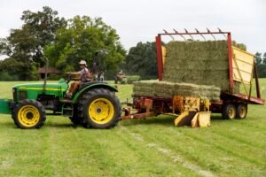 A farmer operating a green tractor loading hay in a rural North Carolina field.