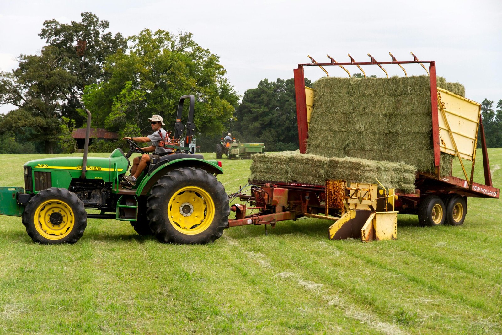 A farmer operating a green tractor loading hay in a rural North Carolina field.